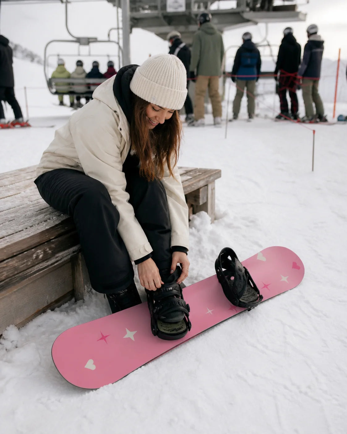 Snowboarder fastening a pink custom snowboard at a chairlift
